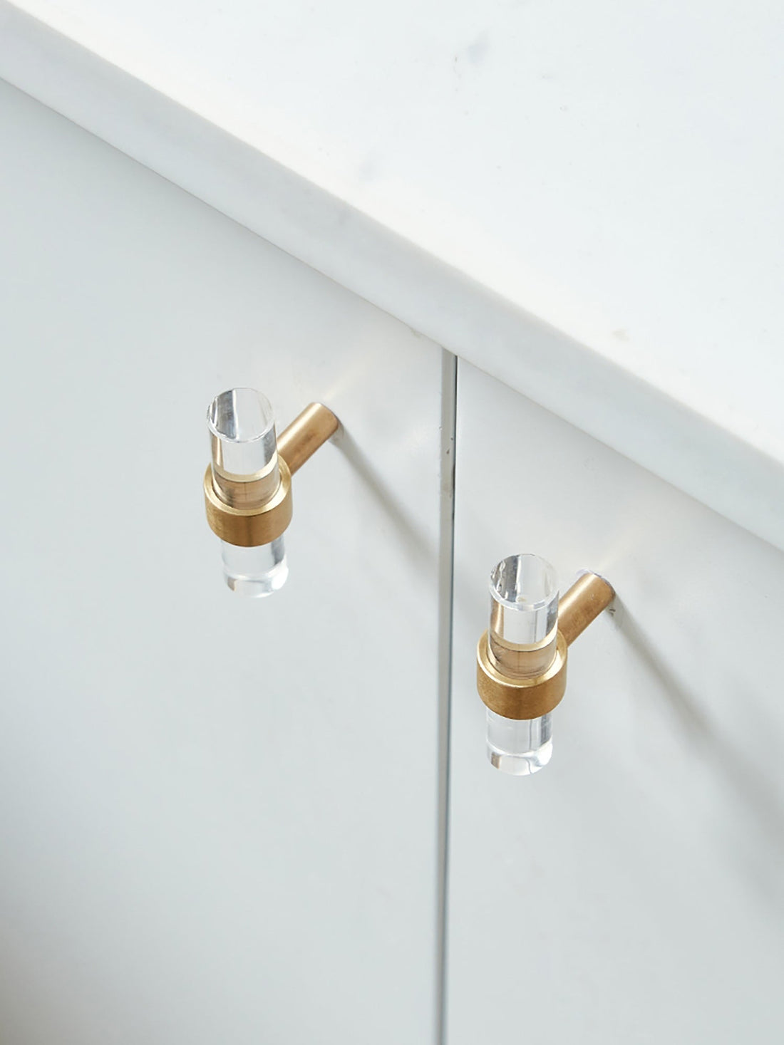A sleek T-bar handle, Petra II made of clear acrylic with brushed brass supports in transparent white finish, model A-0008 by Mantara, A-0008.