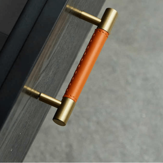 Door handle with a leather grip and brass finish mounted on a wooden door, showcasing a refined and stylish detail by Mantara.