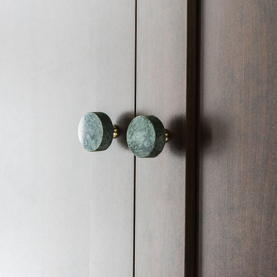  Two round cabinet knobs with a polished finish mounted on a wooden surface, offering a sleek detail by Mantara.