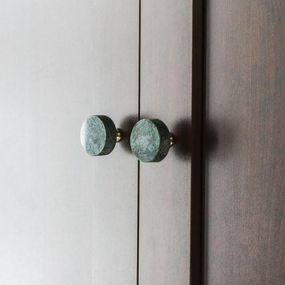  Two round cabinet knobs with a polished finish mounted on a wooden surface, offering a sleek detail by Mantara.