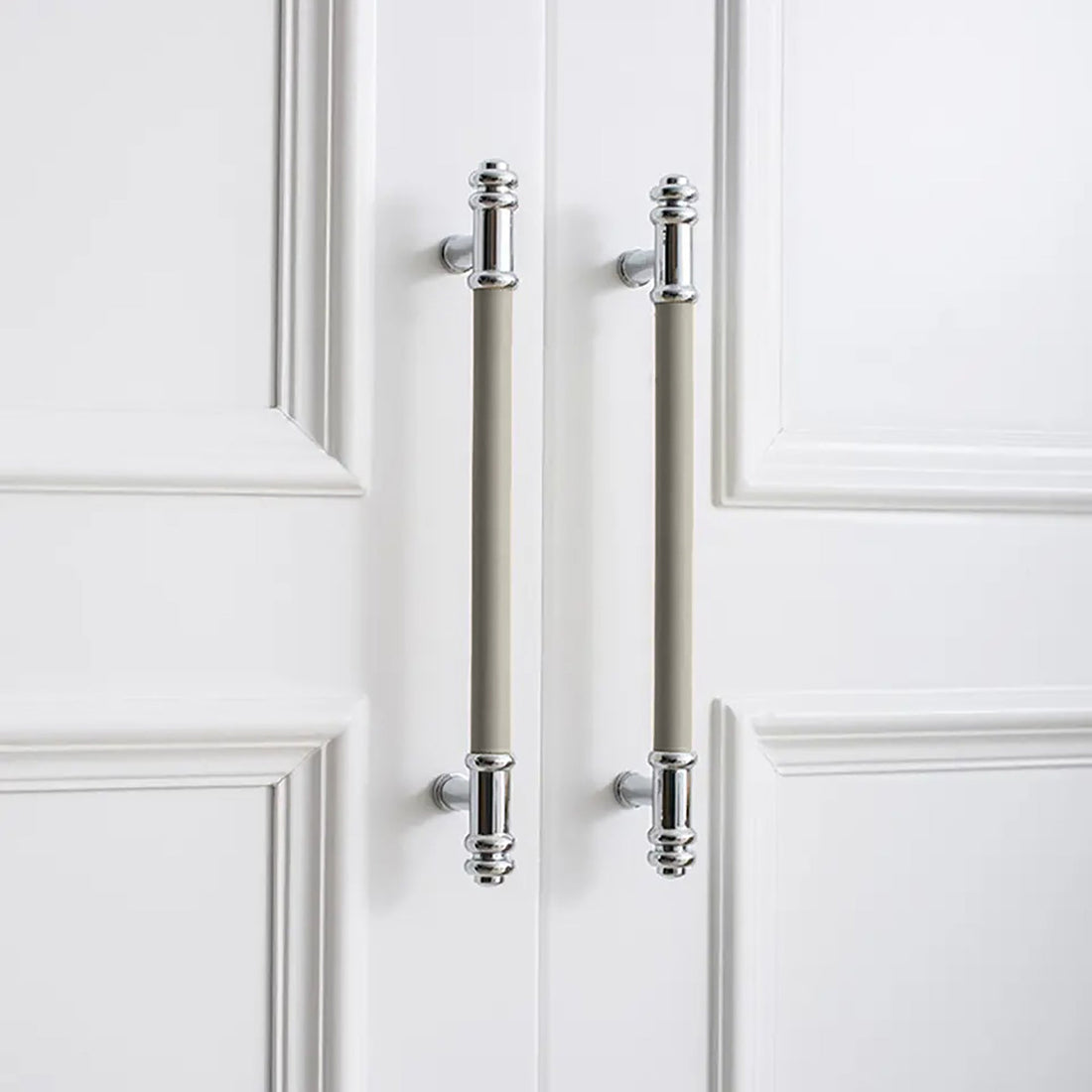 Two vertical silver handles with grey leather grips and a brushed finish, mounted on a white door by Mantara.