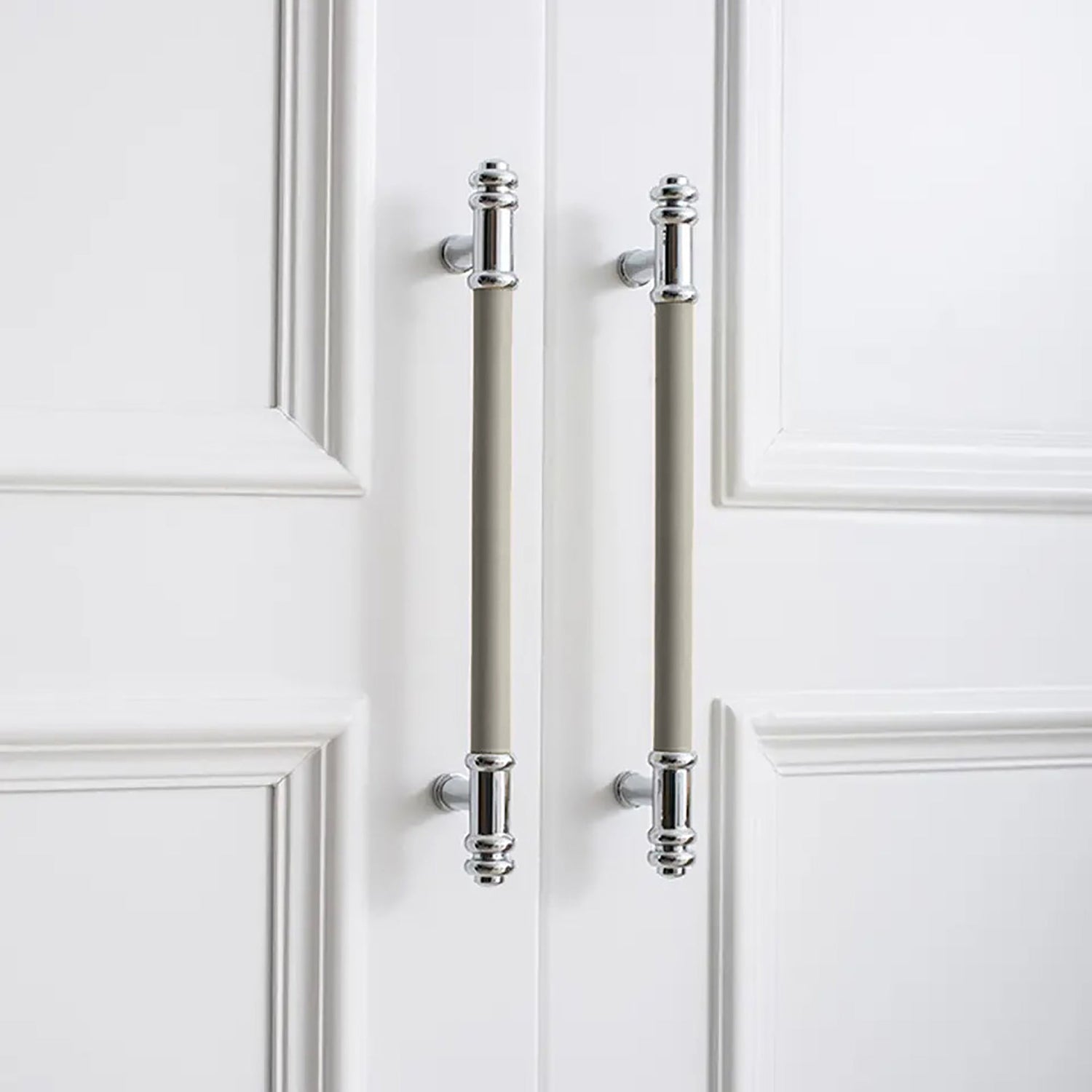 Two vertical silver handles with grey leather grips and a brushed finish, mounted on a white door by Mantara.