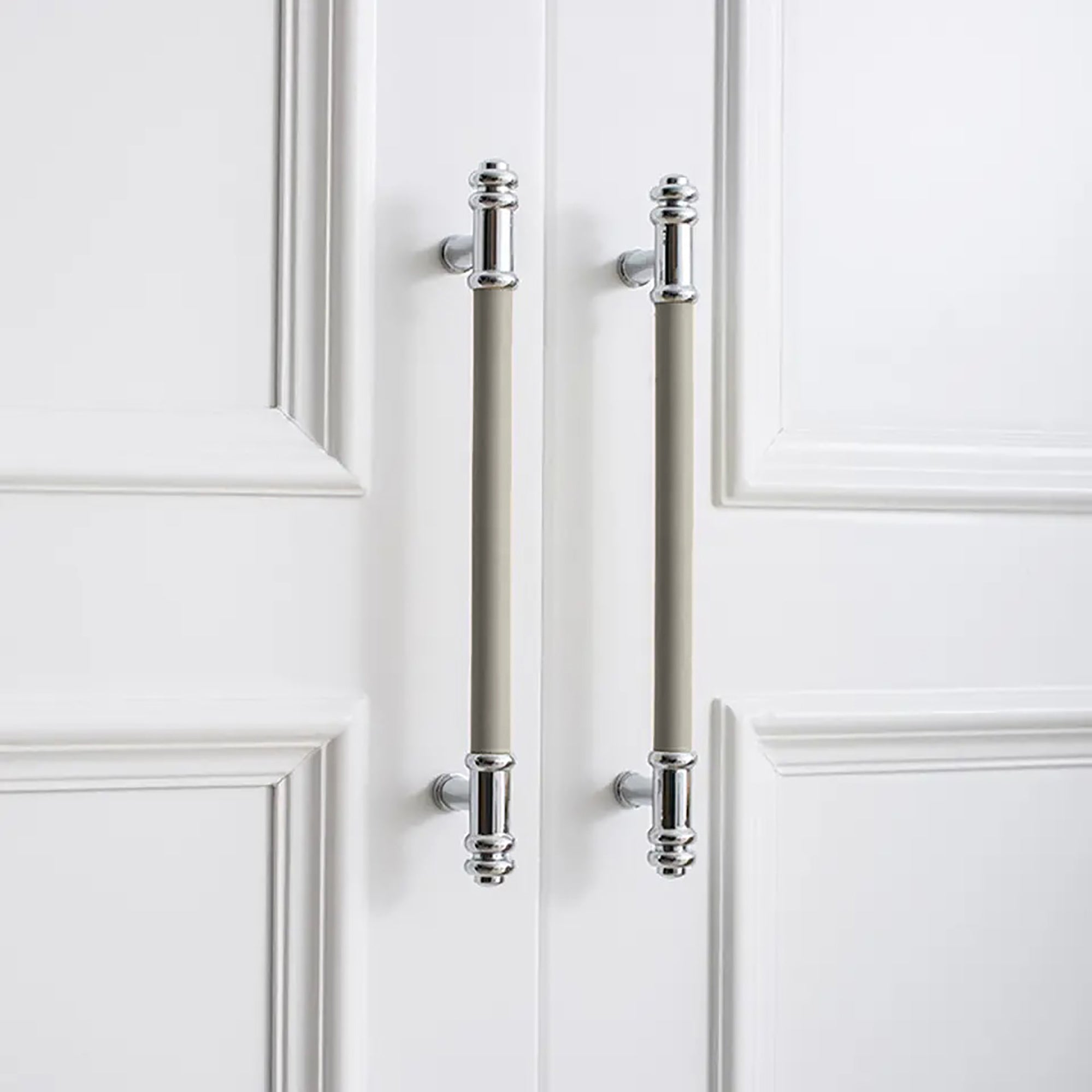 Two vertical silver handles with grey leather grips and a brushed finish, mounted on a white door by Mantara.