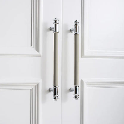 Two vertical silver handles with grey leather grips and a brushed finish, mounted on a white door by Mantara.